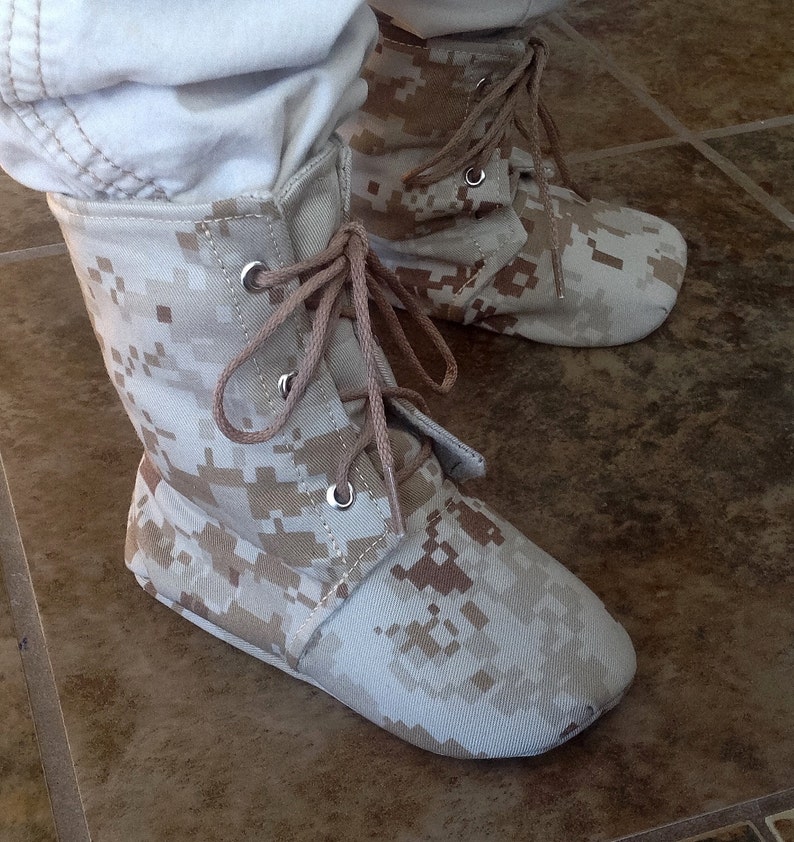 May include: A pair of tan camouflage ankle boots with laces. The boots are made of a canvas-like material and have a low heel.