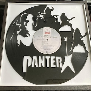 May include: Framed black vinyl record art featuring the band Pantera. The record is cut with silhouettes of band members and the band's name. The record label is visible, with the album title "Vulgar Display of Power". The frame is grey.