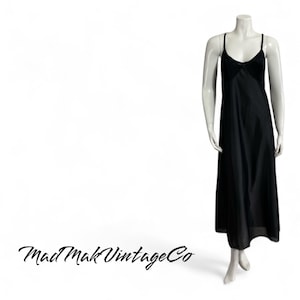 May include: A black slip dress with thin straps and a lace trim at the neckline. The dress is long and flowing, and the model is wearing it against a white background.