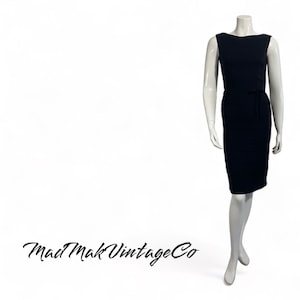 May include: A black sleeveless dress with a fitted silhouette and a tie at the waist. The dress is on a white mannequin.