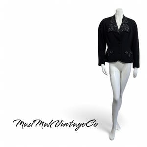 May include: A black blazer with long sleeves and decorative beading on the collar and pockets. The blazer is displayed on a mannequin with white pants. The Mad Mak Vintage Co. logo is in the bottom left corner.