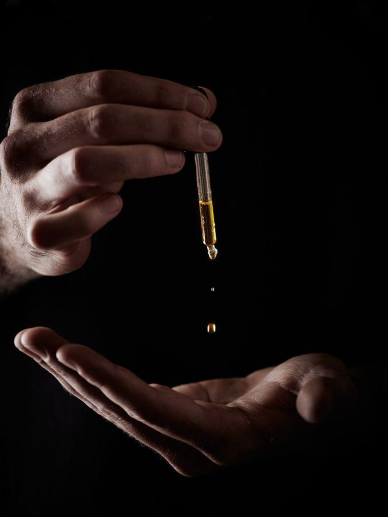 May include: A hand holds a glass dropper with a clear liquid, and a drop falls from the dropper onto an open palm.