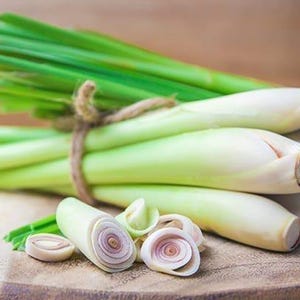 May include: A bunch of fresh lemongrass stalks tied together with twine, with some sliced lemongrass on a wooden cutting board.