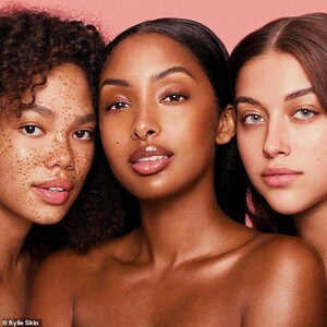 May include: Three women with different skin tones pose for a photo. The woman in the center has dark brown hair and is wearing a light pink lipstick. The woman on the left has curly brown hair and freckles. The woman on the right has long, straight brown hair.
