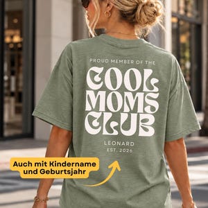 Könnte beinhalten: Ein salbeigrünes T-Shirt mit kurzen Ärmeln und weißem Aufdruck auf der Rückseite: PROUD MEMBER OF THE COOL MOMS CLUB, darunter der Name LEONARD und der Text EST. 2026 in einer kleineren, schlichten serifenlosen Schriftart.