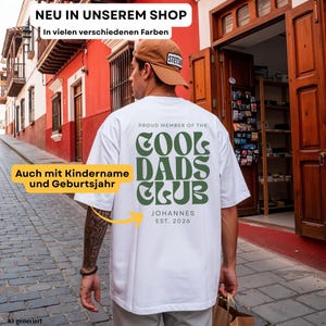 May include: A white t-shirt featuring dark green text on the back that reads PROUD MEMBER OF THE COOL DADS CLUB, with the name JOHANNES and EST. 2026 printed below. The shirt is worn with a tan baseball cap, and the design includes a yellow arrow.