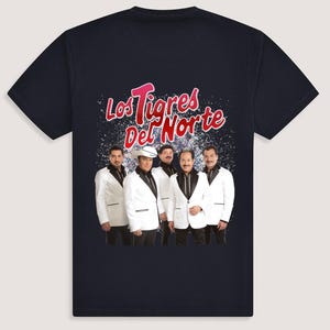 Puede incluir: Una camiseta azul marino con un gráfico blanco de la banda "Los Tigres Del Norte". Los miembros de la banda visten trajes blancos y están de pie frente a un fondo brillante.