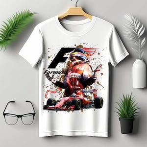 May include: White t-shirt with a graphic print of a Formula 1 race car driver in a red racing suit and helmet, with a red race car and the word "Formula" printed on the shirt.