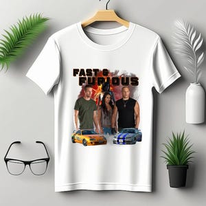 May include: White t-shirt featuring the text "Fast & Furious" above a graphic of the movie's cast and two cars. The graphic includes Paul Walker, Michelle Rodriguez, Vin Diesel, and two sports cars.