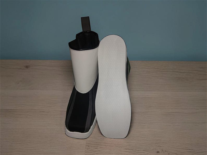 Peut inclure: Une paire de bottes noires, blanches et grises. Une botte est droite, l'autre est couch&eacute;e sur le c&ocirc;t&eacute;, r&eacute;v&eacute;lant la semelle blanche. Les bottes ont un design moderne avec une silhouette montante et une tirette &agrave; l'arri&egrave;re.