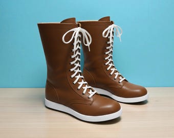 May include: A pair of brown leather boots with white laces and soles. The boots have a mid-calf height and a classic lace-up design. The background is a light blue.