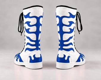 Peut inclure: Une paire de bottes blanches mi-mollet ornées d'un motif bleu en forme de flammes sur les côtés et le bout. Ces bottes présentent des lacets noirs sur le devant, une bordure supérieure noire et une semelle blanche unie, vues côte à côte.