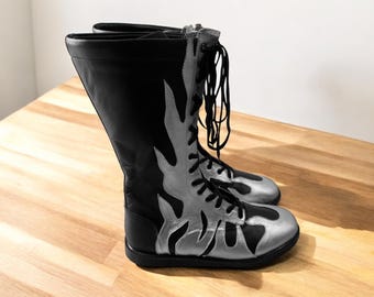 Könnte beinhalten: Schwarze Lederstiefel mit silbernen Flammenmustern und schwarzen Schnürsenkeln. Die Stiefel sind hoch und haben eine spitze Zehenpartie.
