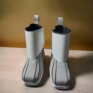 May include: A pair of gray and white ankle boots. The boots have a gray fabric base with vertical black stripes and a white, glossy, fold-over cuff. A gray loop is attached at the back of the cuff. The boots have a white sole.