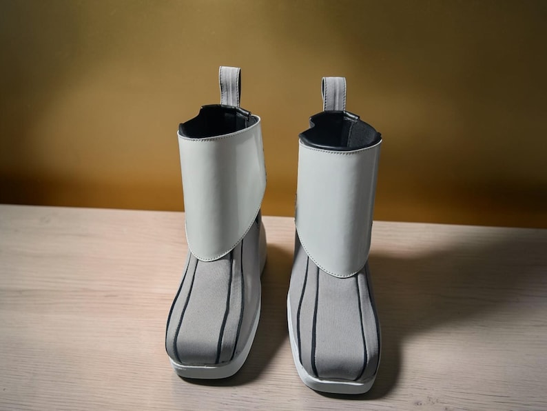 May include: A pair of gray and white ankle boots. The boots have a gray fabric base with vertical black stripes and a white, glossy, fold-over cuff. A gray loop is attached at the back of the cuff. The boots have a white sole.