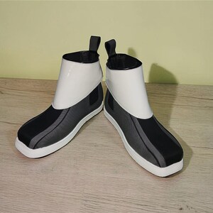 Peut inclure: Une paire de bottines au design moderne. Les bottes pr&eacute;sentent une tige blanche, des accents noirs et gris et une semelle blanche. Elles ont une tirette &agrave; l'arri&egrave;re et une esth&eacute;tique &eacute;pur&eacute;e et minimaliste.