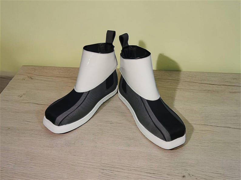 Peut inclure: Une paire de bottines au design moderne. Les bottes pr&eacute;sentent une tige blanche, des accents noirs et gris et une semelle blanche. Elles ont une tirette &agrave; l'arri&egrave;re et une esth&eacute;tique &eacute;pur&eacute;e et minimaliste.