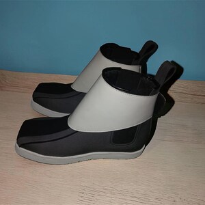 Peut inclure: Une paire de bottines noires et grises au design unique. Les bottines pr&eacute;sentent une bande grise autour de la cheville et une tirette &agrave; l'arri&egrave;re. Les semelles sont grises et les bottines semblent &ecirc;tre faites d'une mati&egrave;re souple.