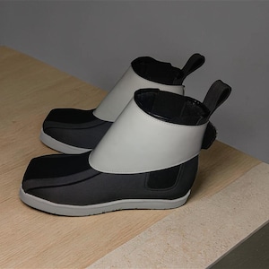 Peut inclure: Paire de bottines noires et grises &agrave; bout carr&eacute;. Elles sont dot&eacute;es d'un large col blanc et d'une tirette &agrave; l'arri&egrave;re. Les semelles sont grises. Les bottines sont pr&eacute;sent&eacute;es sur une surface en bois clair.