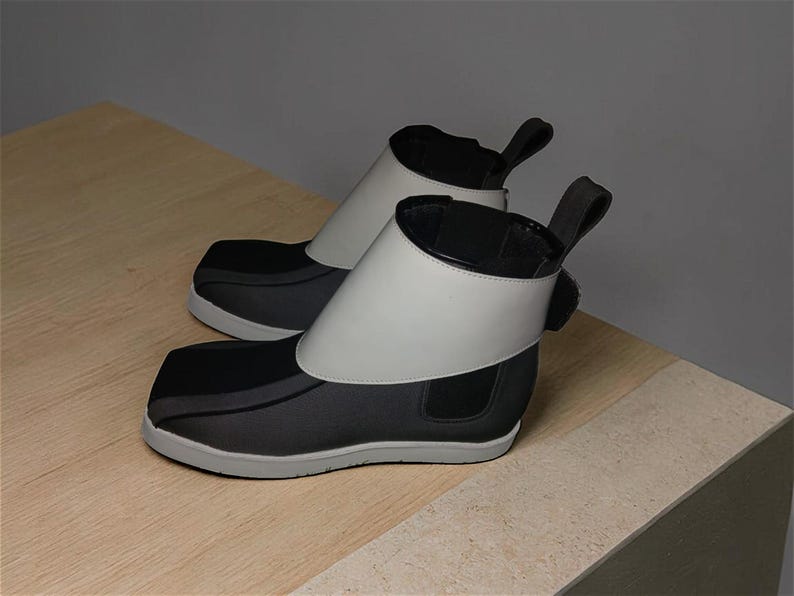 Peut inclure: Paire de bottines noires et grises &agrave; bout carr&eacute;. Elles sont dot&eacute;es d'un large col blanc et d'une tirette &agrave; l'arri&egrave;re. Les semelles sont grises. Les bottines sont pr&eacute;sent&eacute;es sur une surface en bois clair.