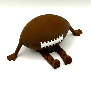 May include: A brown football with white laces, arms, and legs. The arms and legs are articulated, giving the football a playful, anthropomorphic appearance. The football is lying down on a white surface.