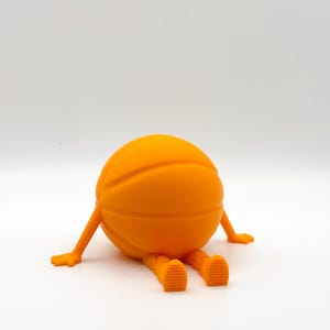 May include: Orange basketball character with arms and legs. The character is sitting on a white surface.