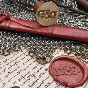 May include: A collection of fantasy items, featuring a dagger with a wooden handle and red leather binding, a gold ring with a red gemstone, and a brass seal with "D&D". Chainmail and red gems are also visible.