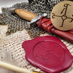 May include: A medieval-themed composition featuring a dagger with a wooden handle, a red leather-wrapped grip, and a metal blade. A brass seal and a red wax seal, both with a stylized emblem, rest on parchment with script, alongside chainmail.