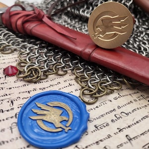 Op de afbeelding: Een close-up van middeleeuwse items, waaronder een rood leren zwaard, maliënkolder en een goudkleurig waszegel met een vogel-embleem. Een blauw waszegel en een rode edelsteen zijn ook zichtbaar.