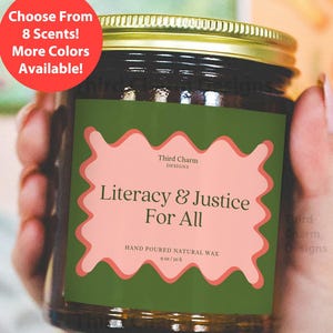 Pode incluir: Uma vela em pote de vidro com tampa dourada e rótulo verde com o texto "Literacy & Justice For All". O rótulo também inclui o texto "Hand Poured Natural Wax" e "9 oz / 50 h". Um círculo vermelho diz "Choose From 8 Scents! More Colors Available!"