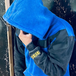 May include: Blue and black color block hoodie with a drawstring hood. The sleeves are black, and the body is blue with a black stripe across the chest. The cuff of the sleeve has the word "INVINC" in yellow.