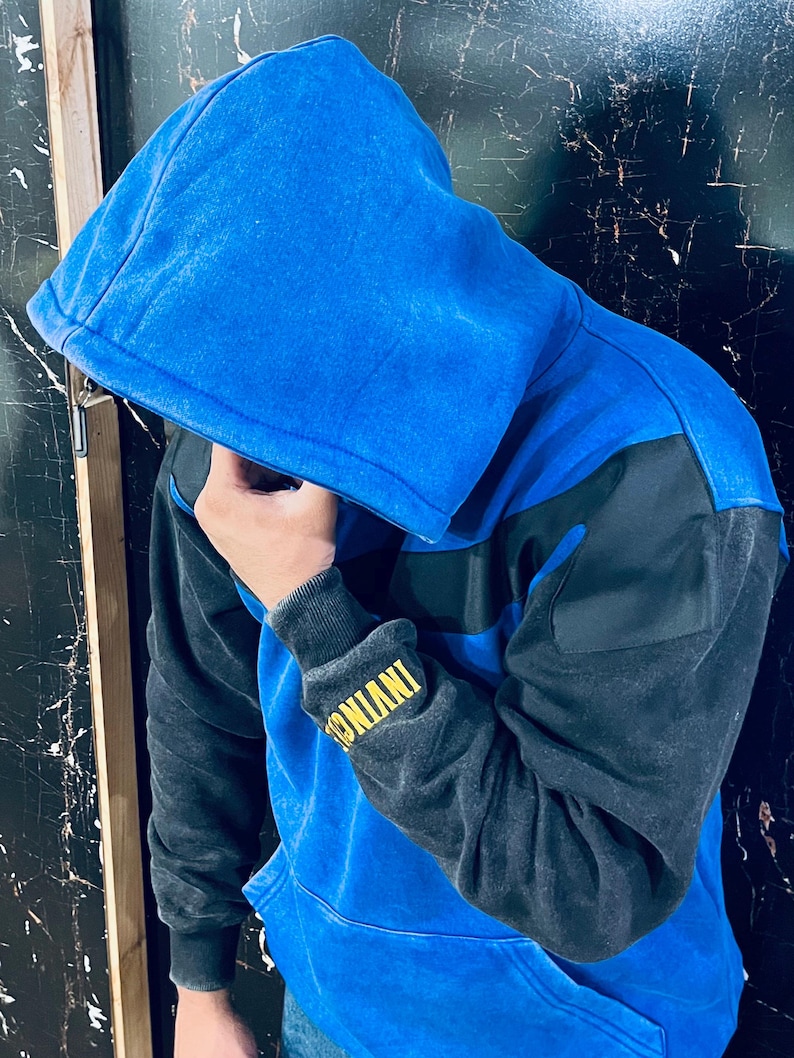 May include: Blue and black color block hoodie with a drawstring hood. The sleeves are black, and the body is blue with a black stripe across the chest. The cuff of the sleeve has the word "INVINC" in yellow.