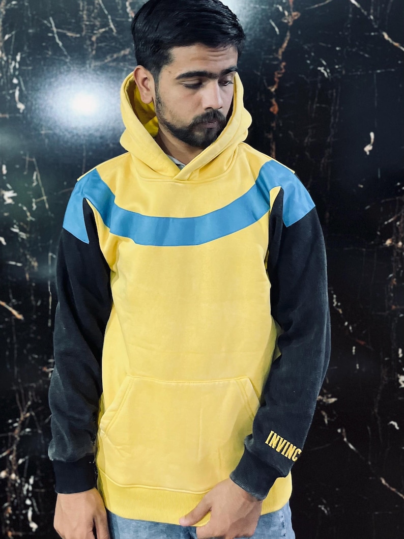 May include: Yellow hoodie with a blue stripe across the chest and black sleeves. The word "INVINC" is printed in gold on the left sleeve. The hoodie has a front pocket and a hood.