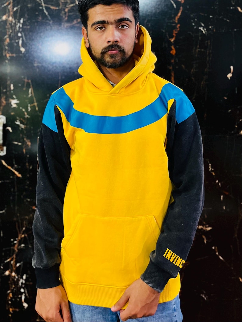 May include: Yellow hoodie with a blue stripe across the chest and black sleeves. The word "INVINC" is printed in yellow on the left sleeve. The hoodie has a front pocket and a hood.