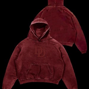 Puede incluir: Una sudadera con capucha granate con un bolsillo delantero y una capucha. La sudadera con capucha presenta un logotipo "DD" en relieve en la parte delantera. La imagen muestra la parte delantera y trasera de la sudadera con capucha sobre un fondo negro.