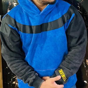 May include: Blue hoodie with black sleeves and a black stripe across the chest. The left sleeve cuff has the word "INVINCIBLE" in yellow lettering. The hoodie has a drawstring hood and a kangaroo pocket.