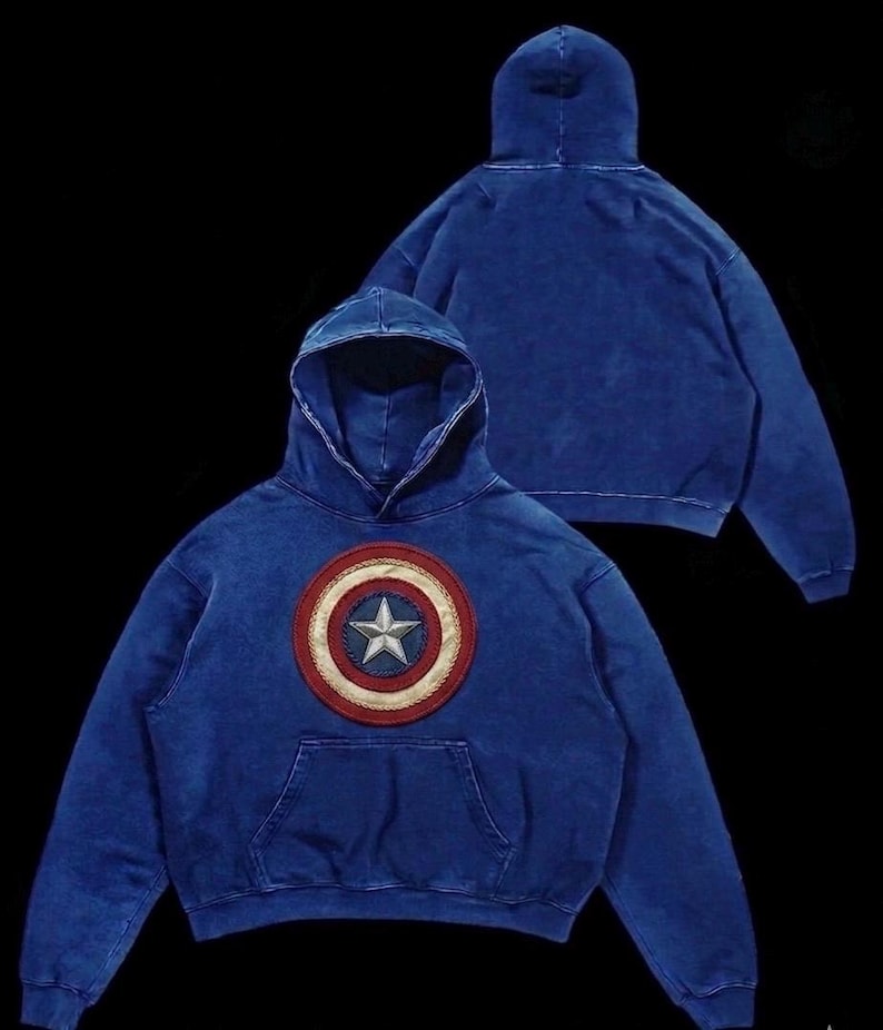 Puede incluir: Sudadera con capucha azul con un escudo del Capit&aacute;n Am&eacute;rica. El escudo es un dise&ntilde;o circular con una estrella blanca en el centro, rodeada de c&iacute;rculos conc&eacute;ntricos rojos, blancos y azules. La sudadera tiene un bolsillo delantero y una capucha con cord&oacute;n.