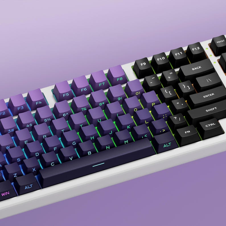 Peut inclure: Un clavier m&eacute;canique blanc avec des touches violettes et noires. Les touches ont des lettres et des symboles blancs. Le clavier pr&eacute;sente un d&eacute;grad&eacute; de couleurs, passant du violet au noir. Le clavier est sur une surface violette.