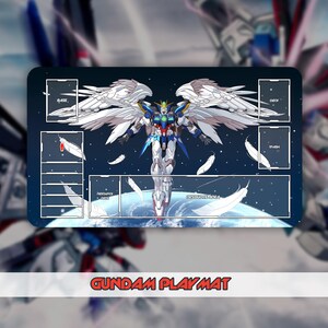 May include: A rectangular Gundam playmat featuring a detailed illustration of a Gundam robot with large white wings, set against a space-themed background. The mat has designated zones for gameplay, with the text "Gundam Playmat" at the bottom.