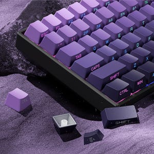 May include: A close-up of a mechanical keyboard with purple gradient keycaps. The keyboard has a black frame and several keycaps are removed, showing the internal components. The keycaps are labelled with letters, numbers, and symbols.