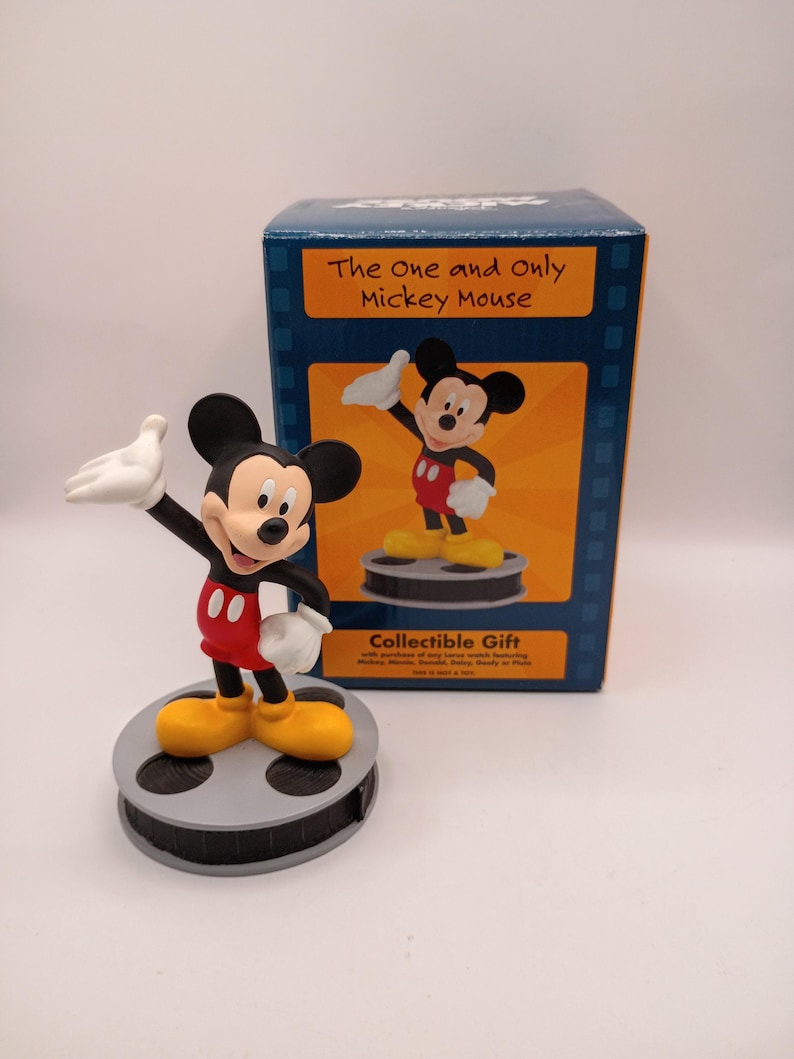 Puede incluir: Una figura de Mickey Mouse en una pose cl&aacute;sica, con pantalones cortos rojos, zapatos amarillos y guantes blancos, se encuentra sobre una base de carrete de pel&iacute;cula. La caja dice "The One and Only Mickey Mouse" y "Collectible Gift".