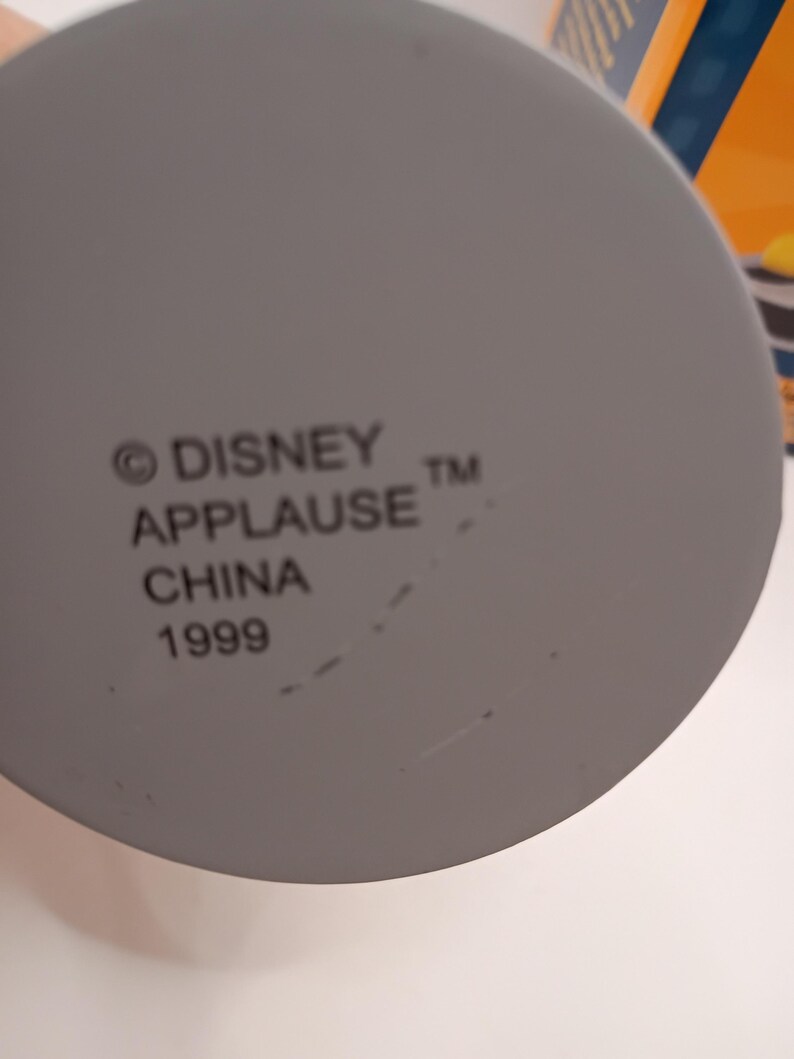 Puede incluir: Primer plano de un objeto gris y circular con el texto "&copy; DISNEY APPLAUSE TM CHINA 1999" impreso. El objeto es probablemente un art&iacute;culo de colecci&oacute;n o parte de un producto m&aacute;s grande.