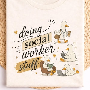 May include: Cream-colored t-shirt with the phrase "doing social worker stuff" and illustrations of ducks. The ducks are depicted in various activities, including reading, working on a laptop, and carrying a coffee cup.