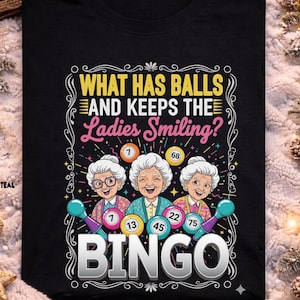 Puede incluir: Camiseta negra con el texto "WHAT HAS BALLS AND KEEPS THE Ladies Smiling?" y la palabra "BINGO". El gráfico presenta a tres mujeres mayores sosteniendo varitas de bingo con números. La camiseta está rodeada de decoraciones festivas.