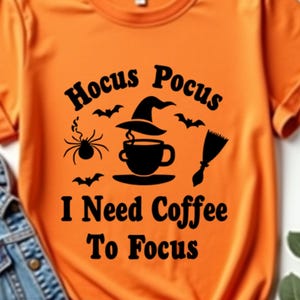 May include: An orange t-shirt with the text "Hocus Pocus I Need Coffee To Focus" in black. The design features a witch's hat, coffee cup, spider, bats, and a broom. A denim jacket is next to the shirt.
