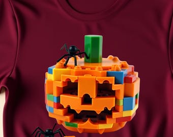 May include: Maroon t-shirt featuring a colorful, block-style pumpkin design with two black spiders. The pumpkin has an orange face and is constructed with various colored blocks. The word "Maroon" is printed in the upper right corner.