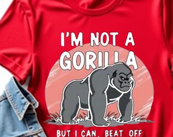 May include: A red t-shirt with the text "I'M NOT A GORILLA BUT I CAN, BEAT OFF A HUNDRED MEN" and a graphic of a gorilla. A denim jacket and a sprig of greenery are next to the shirt.