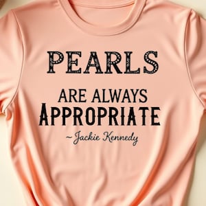 Pode incluir: Uma camiseta cor de pêssego com o texto "PEARLS ARE ALWAYS APPROPRIATE - Jackie Kennedy" impresso em preto.