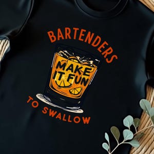 Puede incluir: Camiseta negra con un gráfico de un vaso de zumo de naranja con el texto "Bartenders Make It Fun To Swallow".