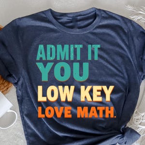 May include: A dark blue t-shirt with the text "ADMIT IT YOU LOW KEY LOVE MATH." in colourful block letters.